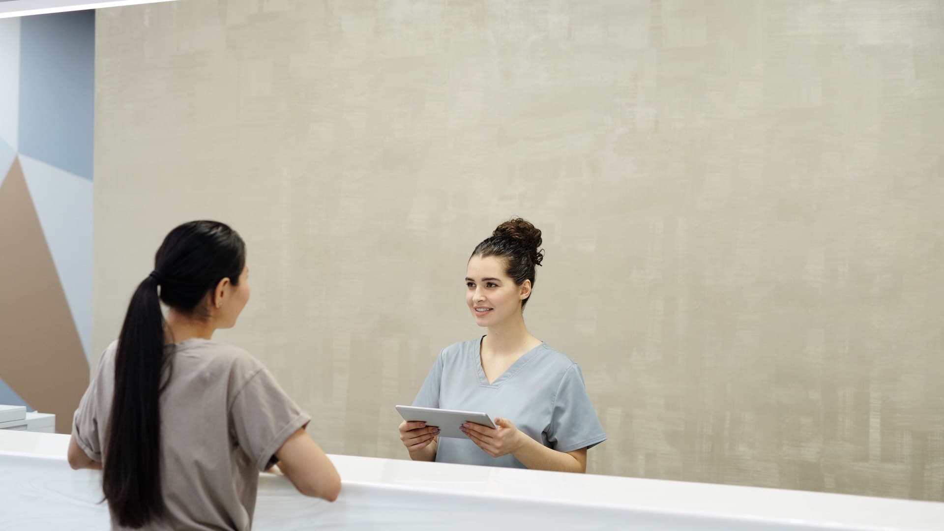 Recepcionista com um tablet atendendo uma paciente no balcao de uma clinica